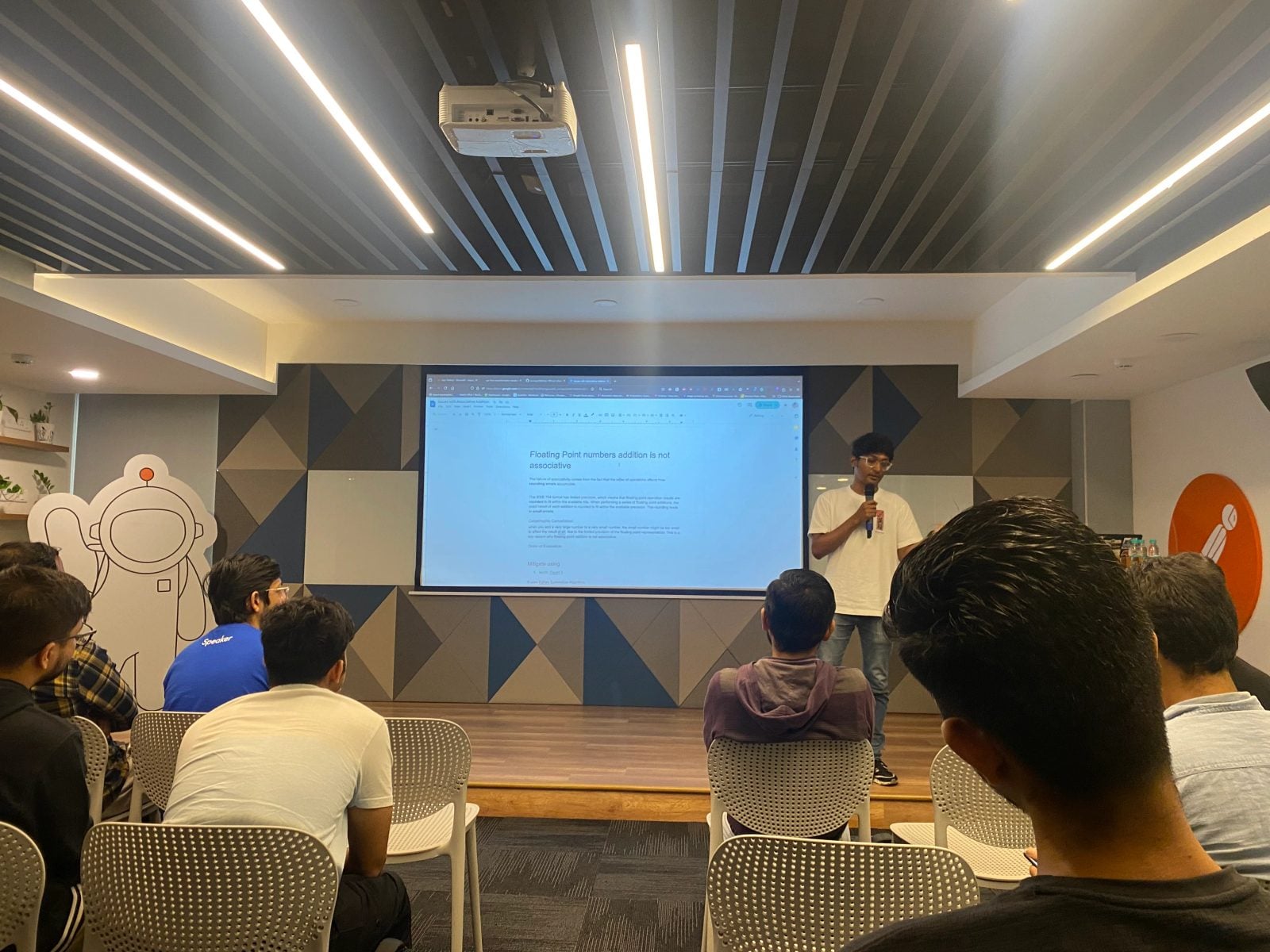Abhik Sarkar giving a lightning talk with a microphone beside a projected document titled "Floating Point numbers addition is not associative" at the BangPypers October 2024 meetup at Postman, Bengaluru